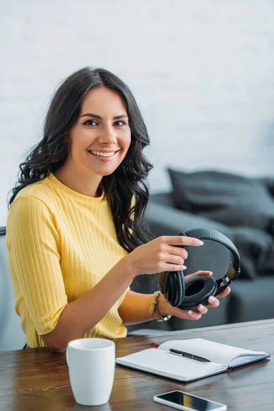 Pretty radio host holding headphones and smiling at camera in broadcasting studio — Stock Photo