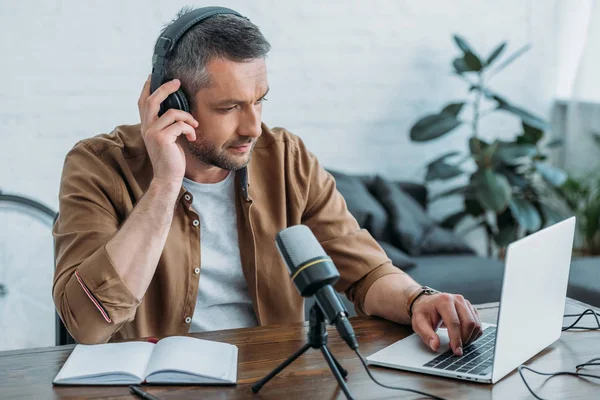 Attentive radio host in headphones using laptop while sitting near microphone — Stock Photo