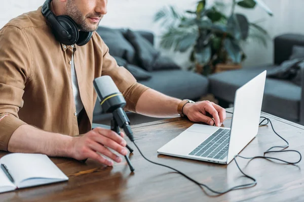 Обрезанный вид радиохоста с помощью ноутбука, сидя рядом с микрофоном — стоковое фото