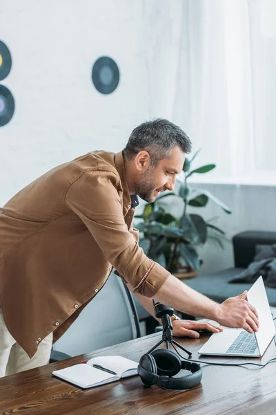 Handsome radio host opening laptop while standing at workplace in broadcasting studio — Stock Photo