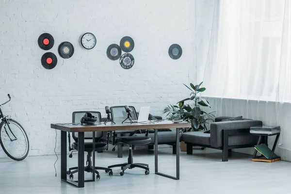 Geräumiges, möbliertes Sendestudio mit Holzschreibtisch, Bürostühlen, Couch und Schallplatten an weißer Wand — Stockfoto