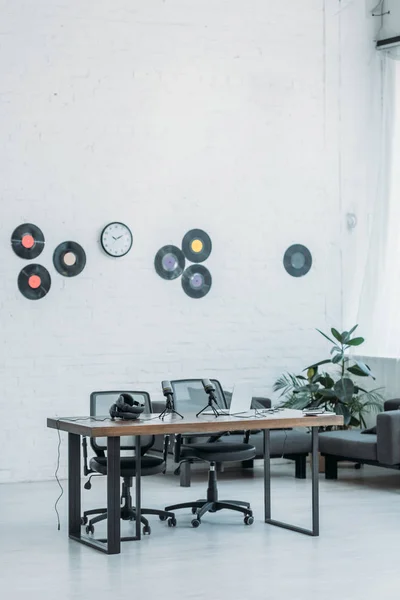 Studio radio spacieux et meublé avec bureau en bois, chaises de bureau et disques vinyle sur mur blanc — Photo de stock