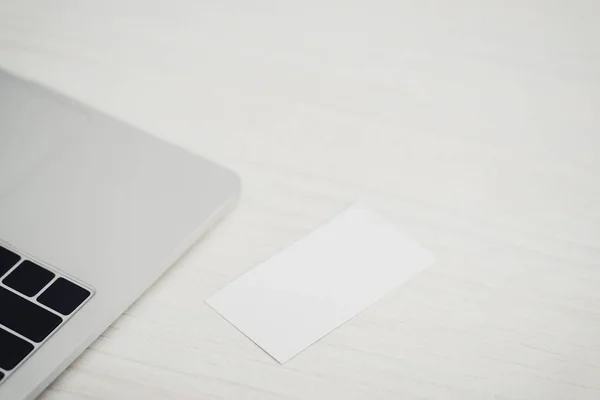 Tarjeta de visita vacía blanca cerca del ordenador portátil en la mesa de oficina de madera - foto de stock