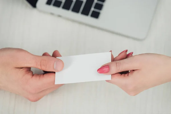 Cropped view of male and female hands with white empty business card near laptop — Stock Photo