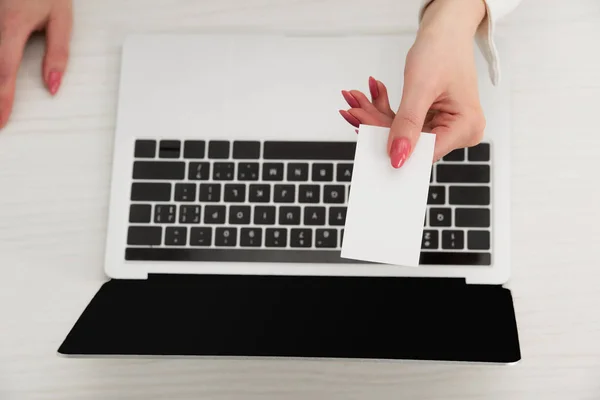 Vista cortada de empresária segurando branco cartão de visita em branco perto do laptop — Fotografia de Stock