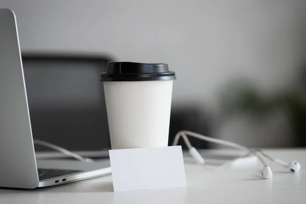 Cartão de visita branco em branco, copo descartável e fones de ouvido na mesa no escritório — Fotografia de Stock