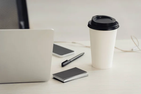 Стопка черных пустых визитных карточек, одноразовая чашка, ноутбук, смартфон и ручка на рабочем столе — стоковое фото