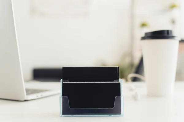 Card holder with black empty business cards near paper cup and laptop on office table — Stock Photo