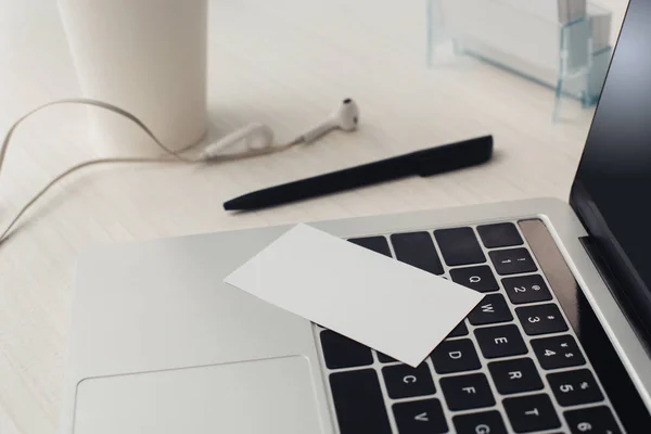 Порожня візитна картка на клавіатурі ноутбука, ручка та навушники на офісному столі — стокове фото