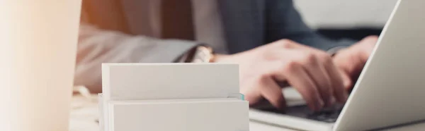 Partial view of businessman using laptop near card holder with blank business cards, panoramic shot — Stock Photo