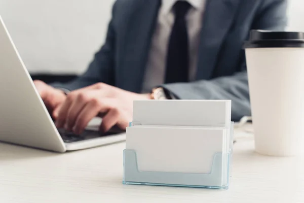 Partial view of businessman using laptop near card holder with empty business cards — Stock Photo