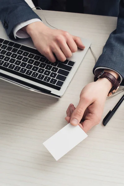 Partial view of businessman holding blank business card while sitting at workplace — Stock Photo