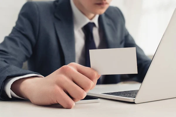 Partial view of businessman showing blank business card at camera while using laptop — Stock Photo