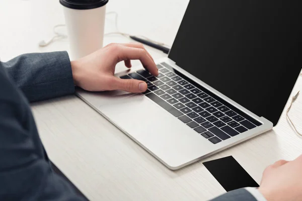 Vista parziale di uomo d'affari utilizzando laptop vicino al caffè per andare e nero biglietto da visita vuoto — Foto stock