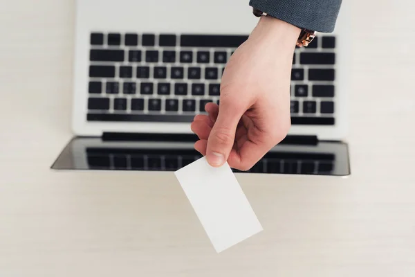 Vue recadrée d'un homme d'affaires tenant une carte de visite vide près d'un ordinateur portable — Photo de stock