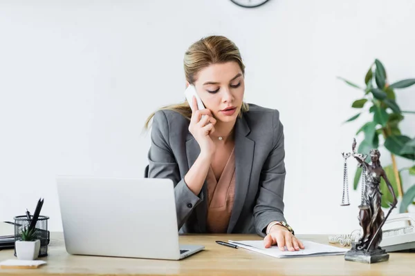 Belle avocate assise au bureau, regardant le document et parlant sur smartphone — Photo de stock