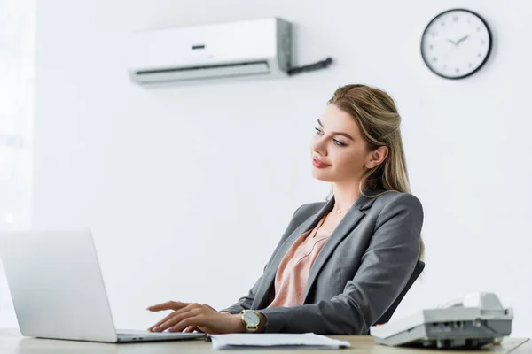 Happy businesswoman sitting in office with air conditioner and usinglaptop — Stock Photo