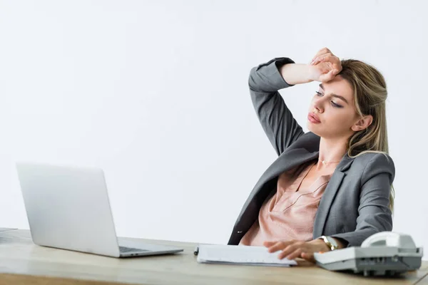Mulher de negócios sentada no escritório, sofrendo de calor, olhando para longe e segurando a mão perto do rosto — Fotografia de Stock