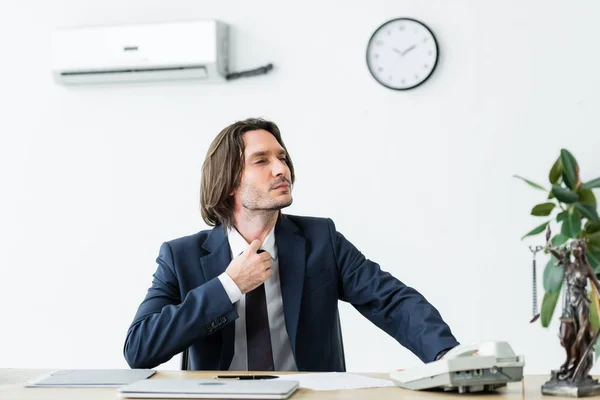 Бизнесмен сидит в офисе, смотрит в сторону и страдает от жары — стоковое фото