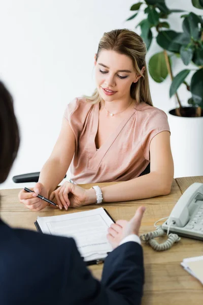 Mujer feliz sentado en la oficina brillante con hombre de negocios y la firma de contrato - foto de stock