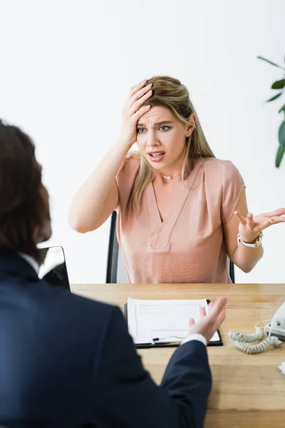 Selective focus of frustrated woman looking at businessman and holding hand on head — Stock Photo