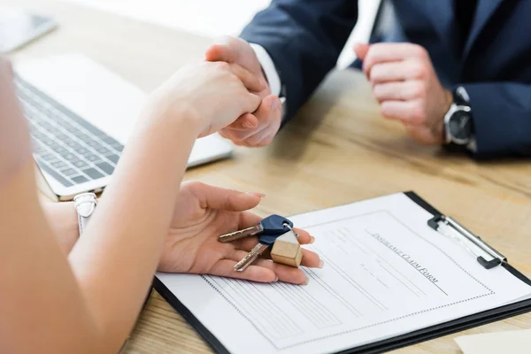 Vue recadrée de la femme tenant les clés dans la main et serrant la main avec l'agent immobilier — Photo de stock