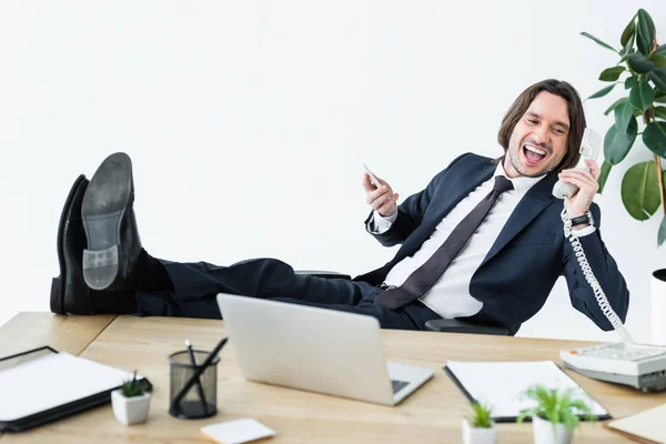 Happy businessman talking on telephone, holding smartphone and headset in hands — Stock Photo