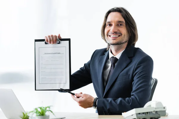 Feliz empresario sosteniendo el formulario de reclamación de seguro en la mano y mirando a la cámara - foto de stock