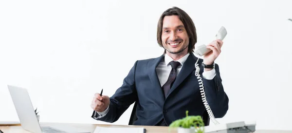 Plano panorámico de hombre de negocios feliz con auriculares en la mano y mirando a la cámara - foto de stock