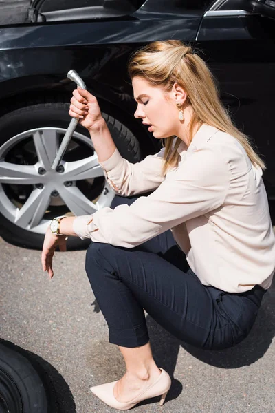 Bouleversé femme d'affaires avec outil à la main assis près de cassé auto, concept d'assurance automobile — Photo de stock