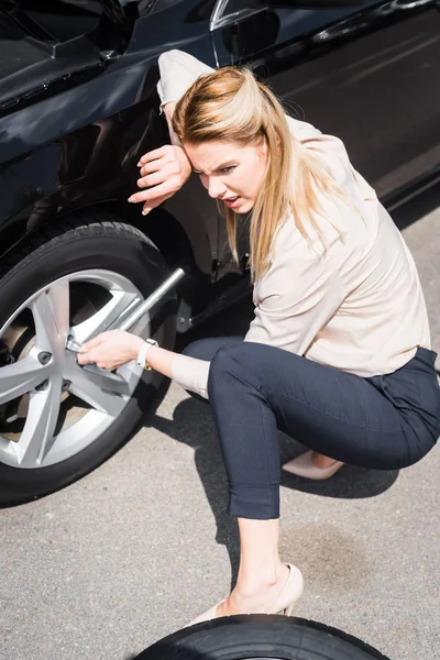 Tired businesswoman with tool in hand sitting near broken auto, car insurance concept — Stock Photo