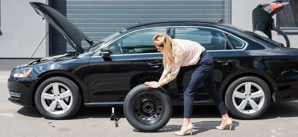 Donna d'affari rotolamento nuova ruota e fissaggio rotto auto, concetto di assicurazione auto — Foto stock