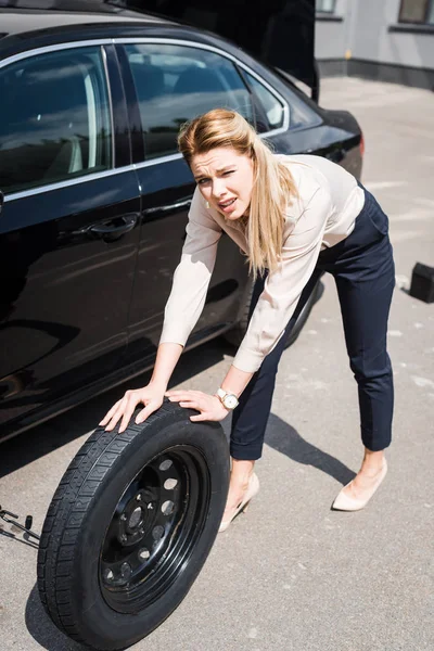 Businesswoman looking at camera, rolling new wheel and fixing broken auto, car insurance concept — Stock Photo