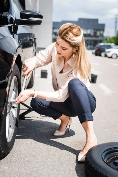 Бізнес-леді фіксує колесо на зламаному автомобілі, концепція страхування автомобілів — стокове фото