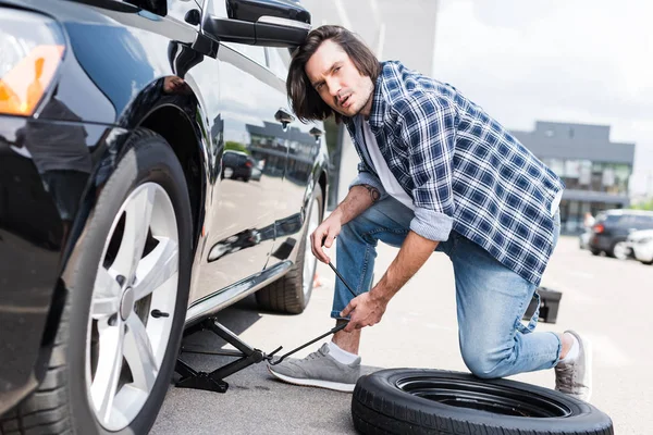 Hombre usando la herramienta del gato y fijar auto roto, concepto de seguro de coche - foto de stock