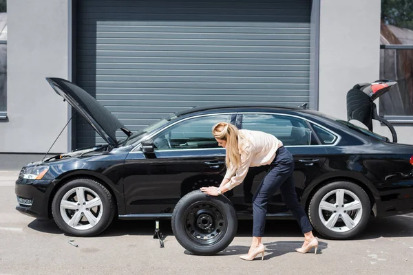 Бізнес-леді котиться нове колесо і фіксує зламаний автомобіль, концепція страхування автомобілів — стокове фото