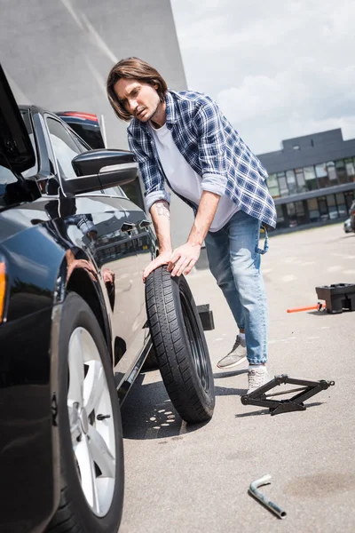 Hombre rodando nueva rueda y la fijación de automóviles rotos, concepto de seguro de coche - foto de stock