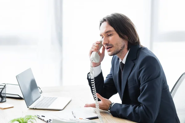 Uomo d'affari parlare al telefono, seduto in ufficio e guardando altrove — Foto stock