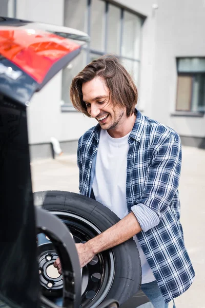 Щасливий чоловік тримає колесо в руках біля автомобіля, концепція страхування автомобілів — стокове фото