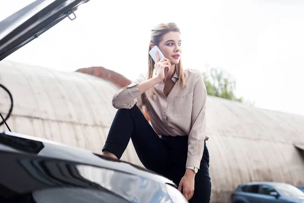 Mujer de negocios hablando en el teléfono inteligente cerca de auto roto y mirando hacia otro lado, concepto de seguro de coche - foto de stock