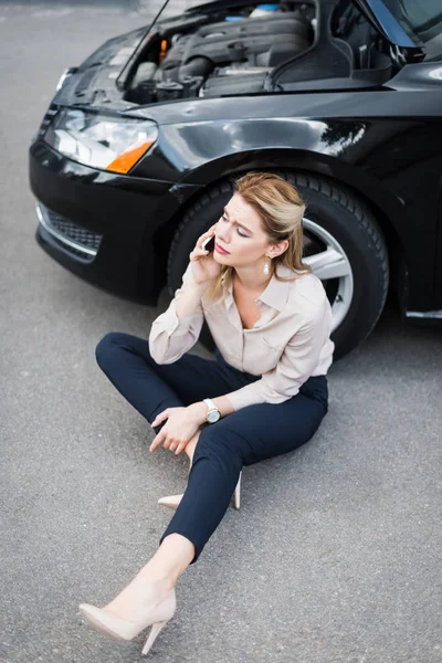 Schöne Geschäftsfrau, die auf dem Smartphone spricht und in der Nähe eines kaputten Autos sitzt, Kfz-Versicherungskonzept — Stockfoto