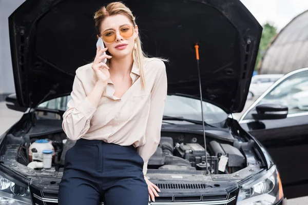 Businesswoman talking on smartphone near broken auto with open trunk, car insurance concept — Stock Photo