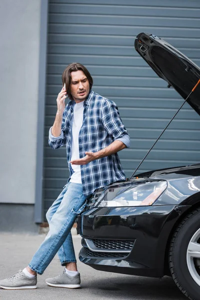 Man talking on smartphone near broken auto with open trunk, car insurance concept — Stock Photo