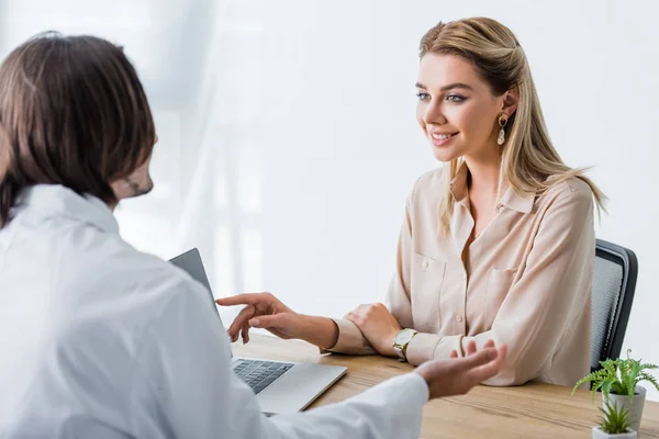 Schön lächelnde Patientin schaut Arzt an und zeigt mit dem Finger auf Laptop — Stockfoto