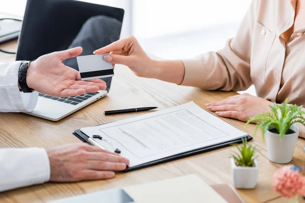 Ausgeschnittene Ansicht des Patienten am Tisch mit Antragsformular der Versicherung, das dem Arzt die Kreditkarte gibt — Stockfoto