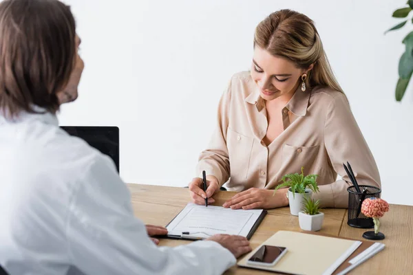 Beautiful woman signing insurance claim form near doctor in clinic — Stock Photo