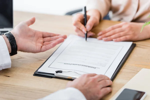 Vista recortada de la mujer que firma formulario de reclamación de seguro cerca del médico en la clínica — Stock Photo