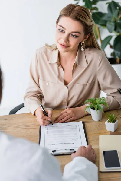 Selective focus of beautiful patient signing document and looking at doctor — Stock Photo