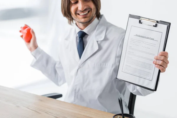Médico feliz segurando coração vermelho e formulário de pedido de seguro em mãos — Fotografia de Stock