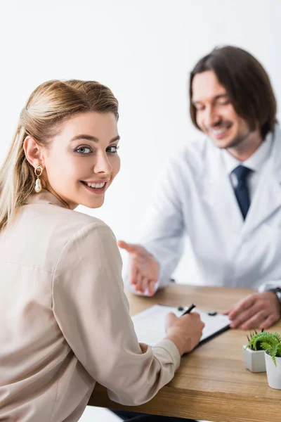 Beautiful patient visiting doctor, looking at camera and signing document — Stock Photo